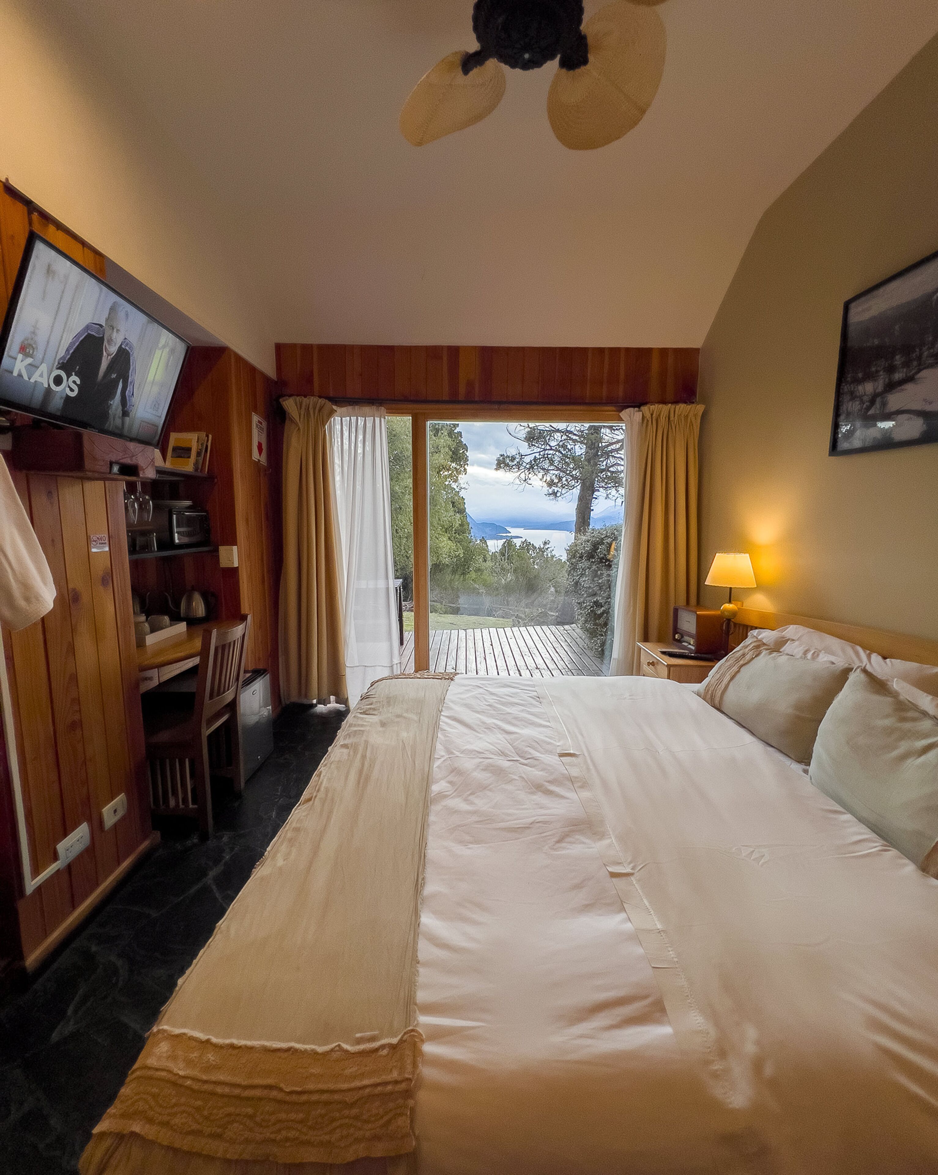 A hotel room with a large bed, a desk with a TV, and a view of the outdoors.
