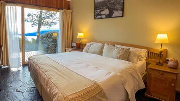 A bedroom with a large bed, two bedside tables with lamps, a painting on the wall, and a view of the outdoors.