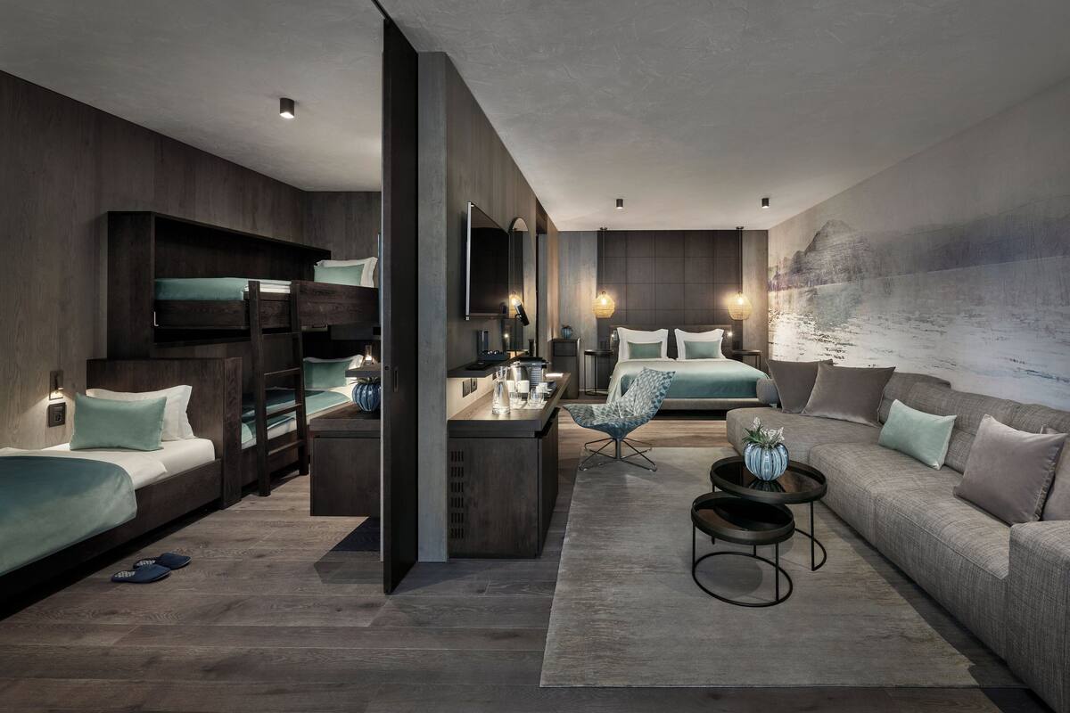 Una habitación de hotel moderna con una cama litera, un sofá, un comedor y un gran mural en la pared.
