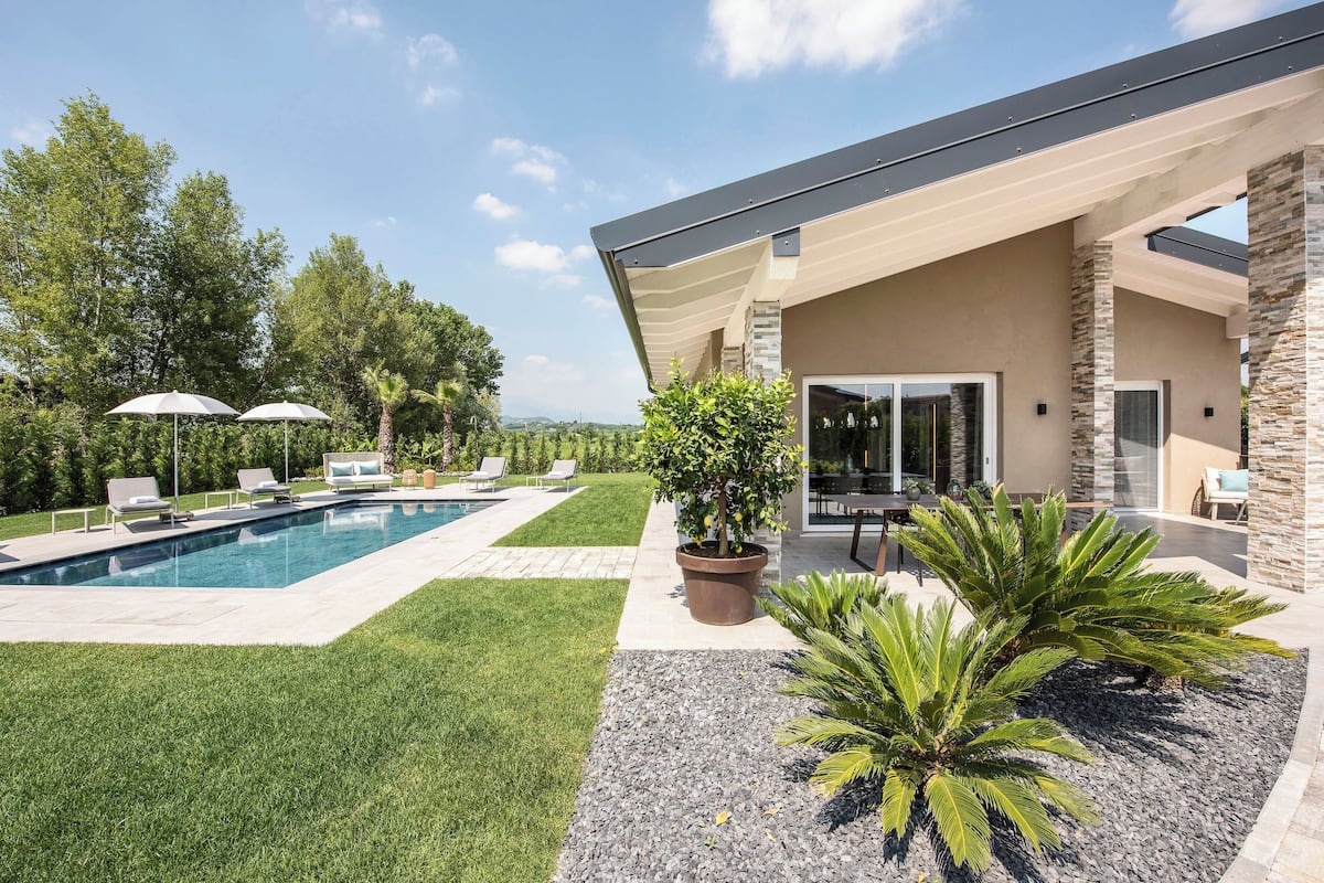 Una casa moderna con piscina, mobiliario exterior y un césped cuidado.