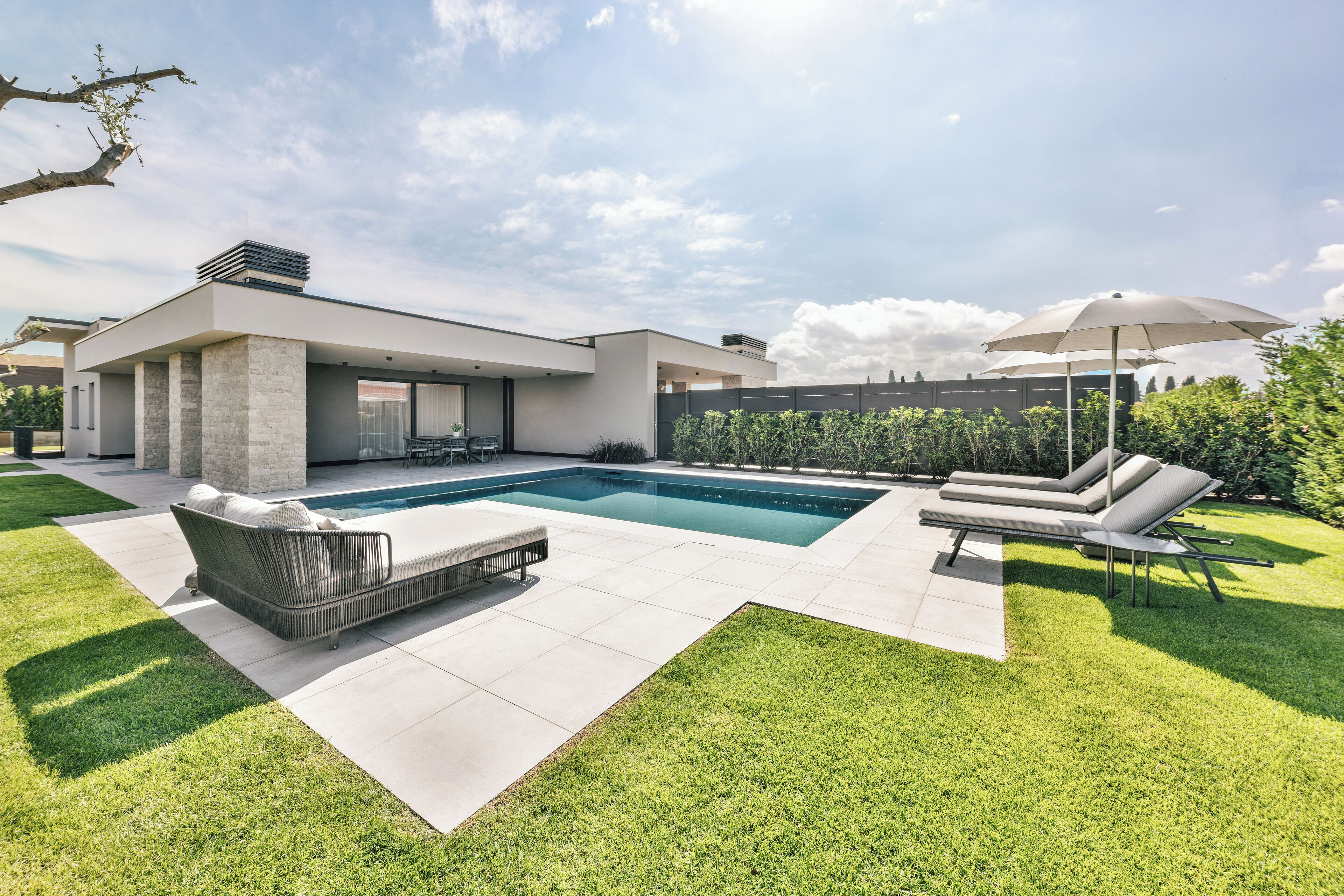 A modern house with a swimming pool, outdoor seating, and a well-maintained lawn.