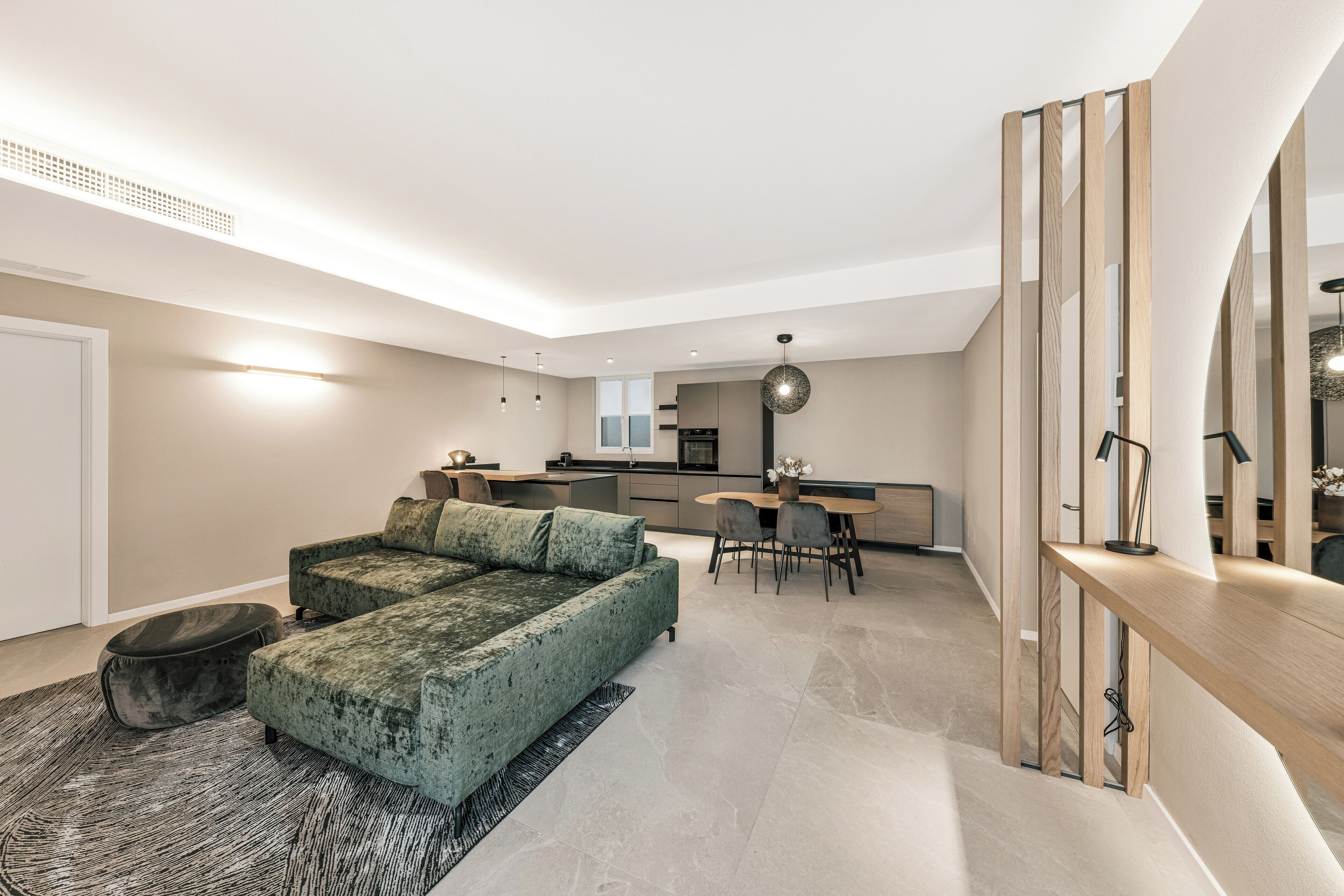 Ein modernes Wohnzimmer mit einem grünen Sofa, einem Essbereich mit Tisch und Stühlen sowie einer Küche im Hintergrund.