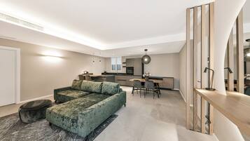 A modern living room with a green sofa, a dining area with a table and chairs, and a kitchen in the background.