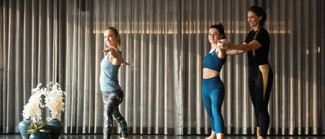 Tres personas sobre esterillas de yoga en una habitación con un telón de fondo y plantas decorativas.