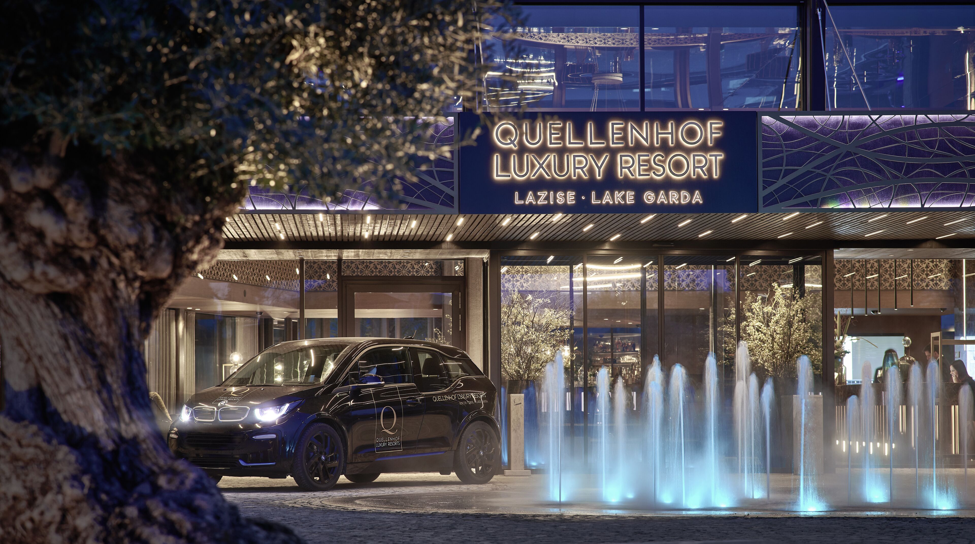A luxury resort entrance with a car parked in front, a signboard, and a fountain display.