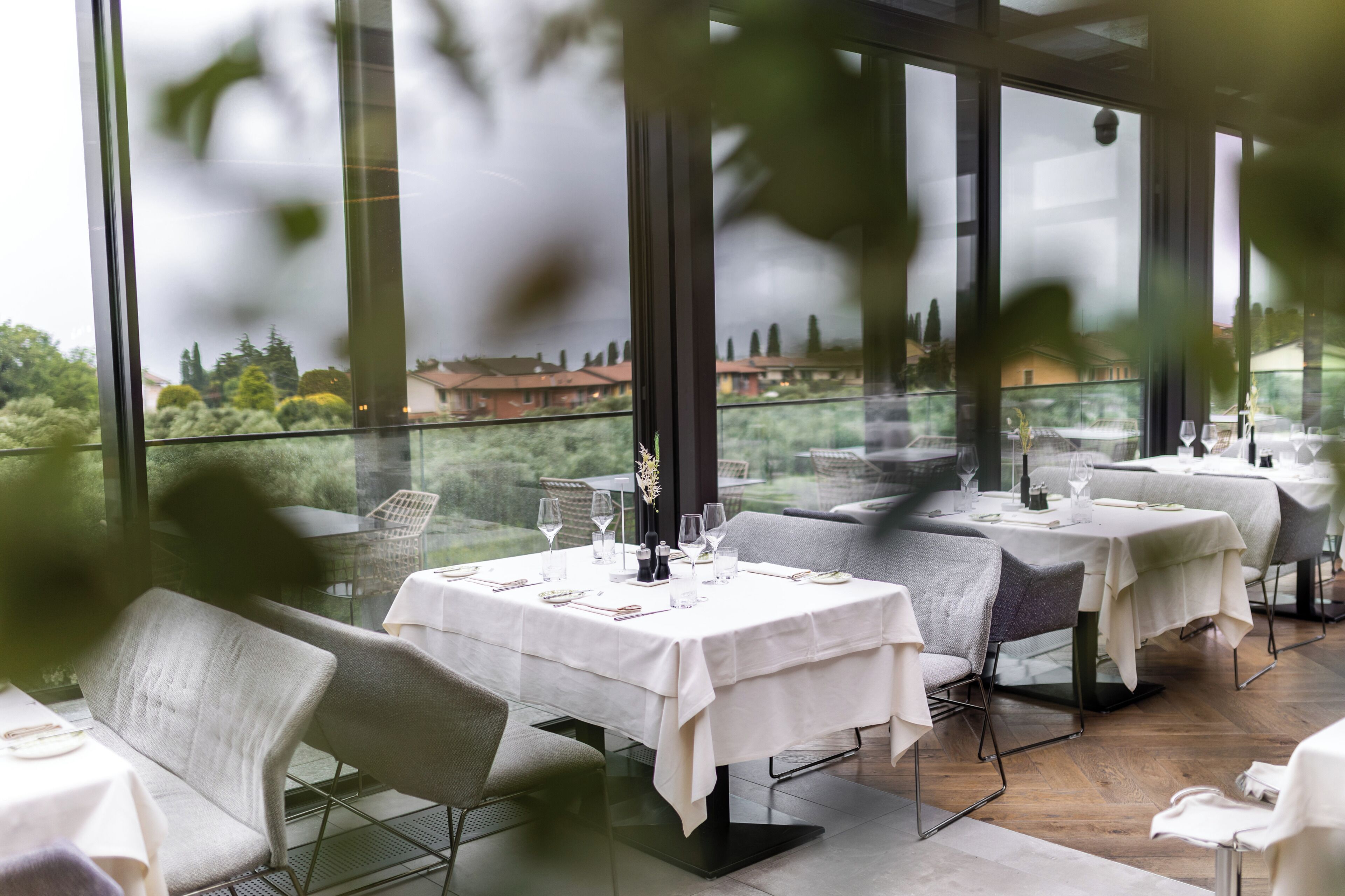 A restaurant with tables set for dining, large windows, and a view of greenery and buildings.
