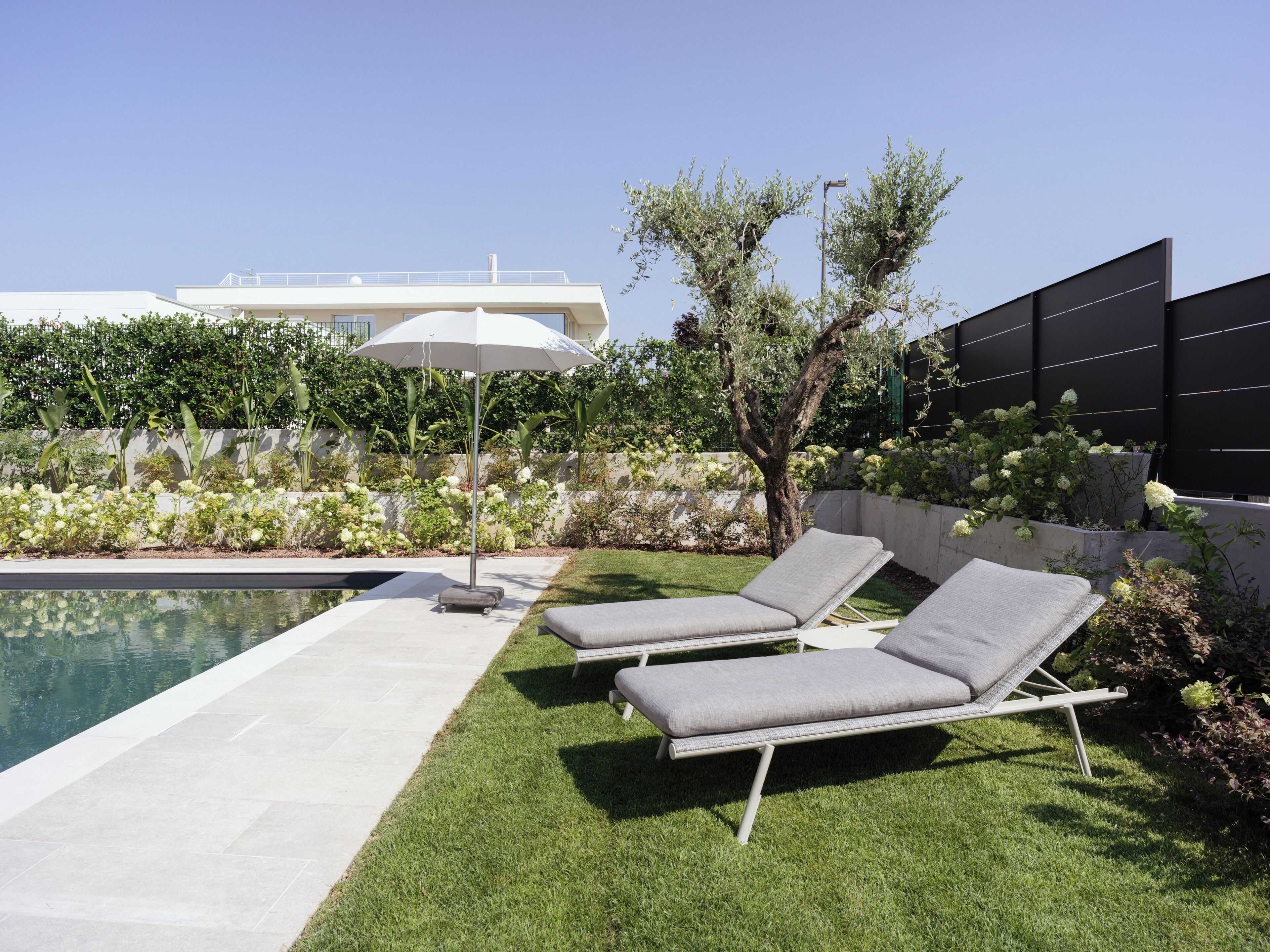 Ein moderner Poolbereich im Freien mit zwei Liegestühlen und einem großen Sonnenschirm.