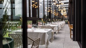 Un restaurante con mesas dispuestas para comer, ventanas amplias y lámparas colgantes.