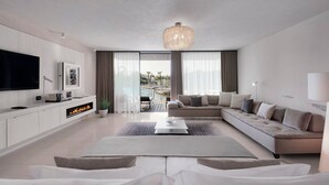 Una sala de estar moderna con televisor de pantalla plana, chimenea, sofá y vistas a una piscina y palmeras.