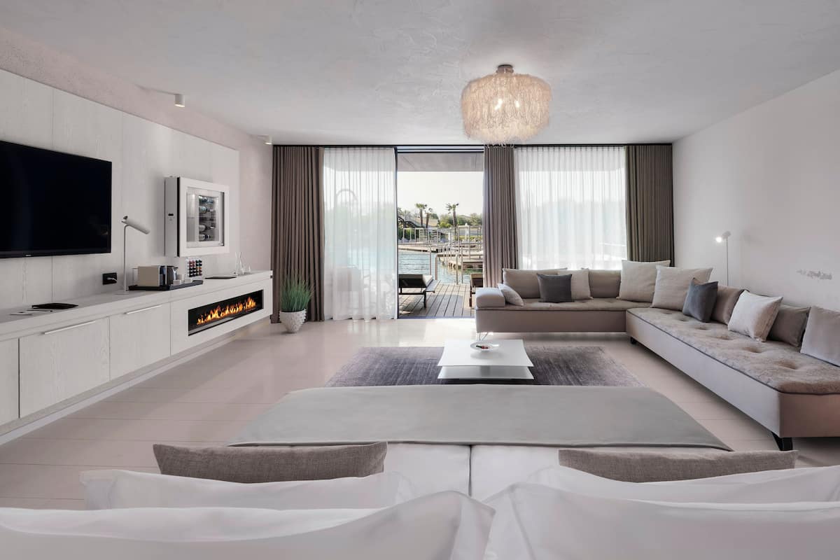 Una sala de estar moderna con televisor de pantalla plana, chimenea, sofá y vistas a una piscina y palmeras.