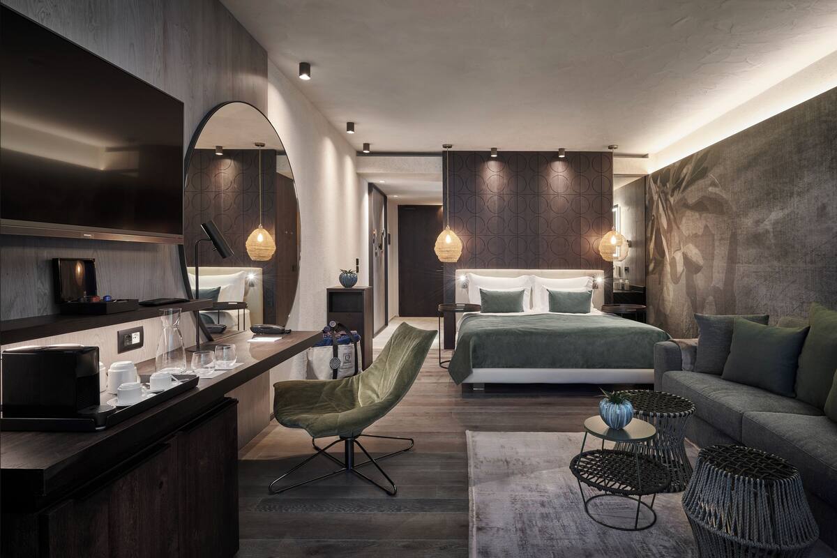 Una habitación de hotel moderna con cama, sofá, zona de comedor y pequeña cocina.