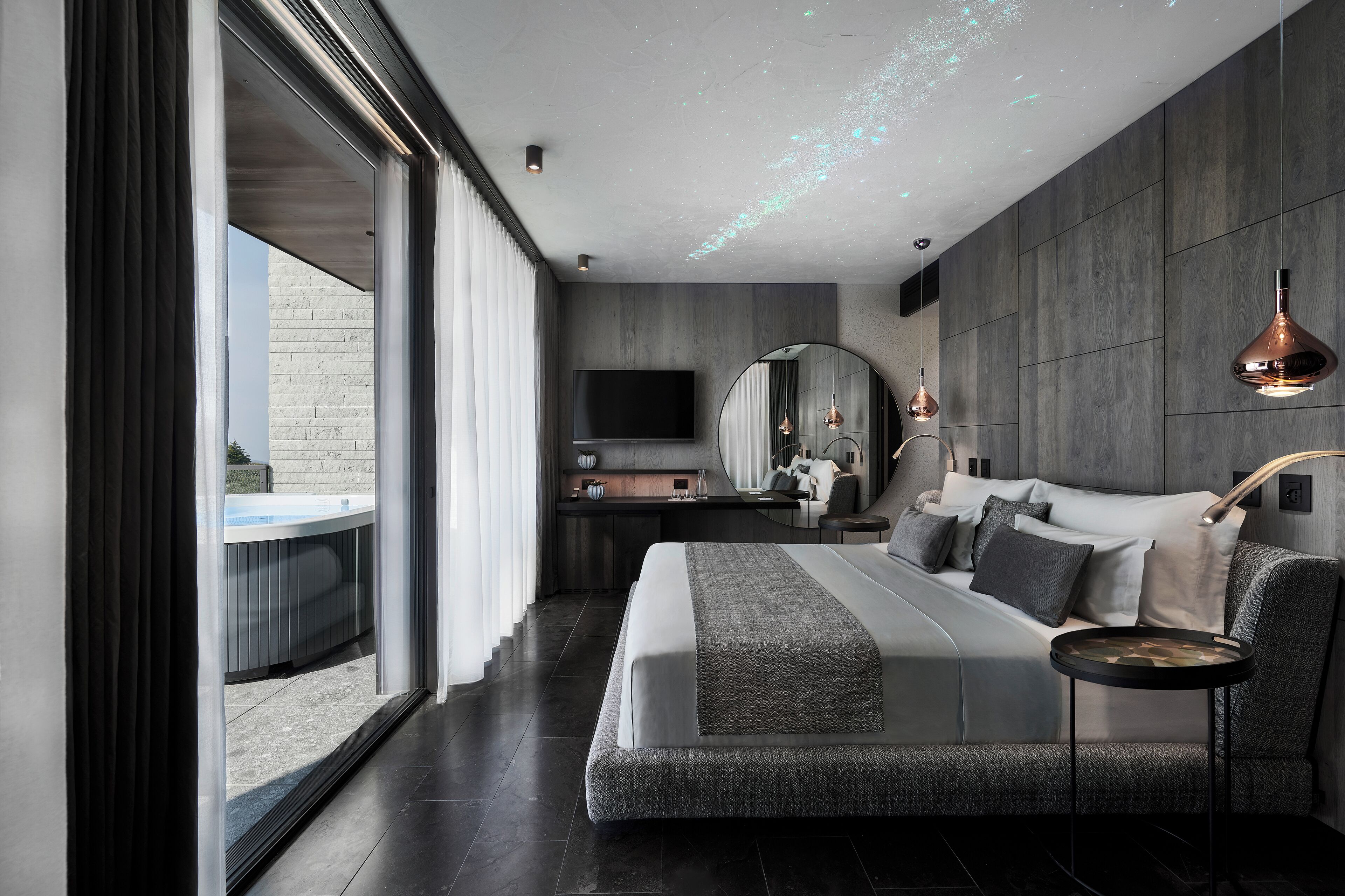 A modern bedroom with a large bed, a TV, a desk, and a view of the outdoors.