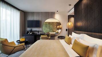 Une chambre d’hôtel moderne dotée d’un grand lit, d’un bureau avec un téléviseur à écran plat, d’un miroir rond et d’un coin salon avec des fauteuils et une petite table.