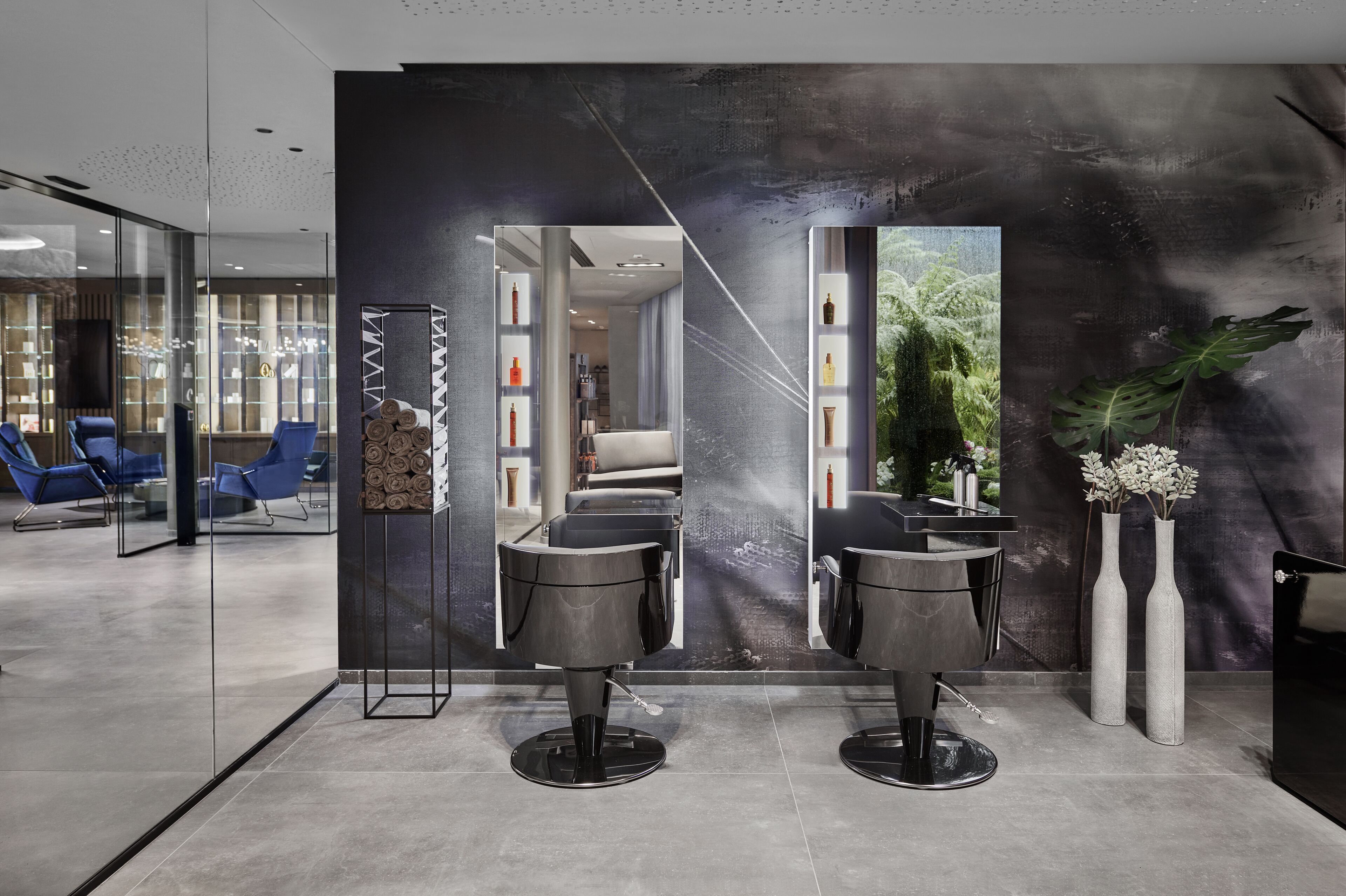 Un salón moderno con dos sillones de peluquería negros, una mampara de vidrio y un espejo grande.