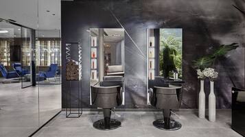 A modern salon with two black salon chairs, a glass partition, and a large mirror.