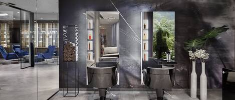 Un salón moderno con dos sillones de peluquería negros, una mampara de vidrio y un espejo grande.