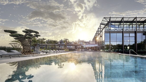 Un hotel moderno con piscina cristalina, sillones de descanso y una estructura de vidrio.