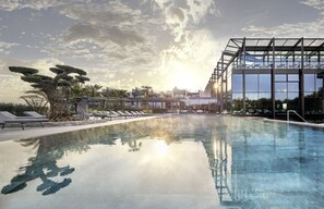 A modern hotel with a clear pool, lounge chairs, and a glass-enclosed structure. - Quellenhof Luxury Resort Lazise (Lazise)