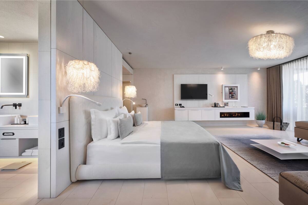 Un dormitorio moderno con una cama grande, mesitas de noche, un televisor y un rincón de descanso con una mesa de centro.