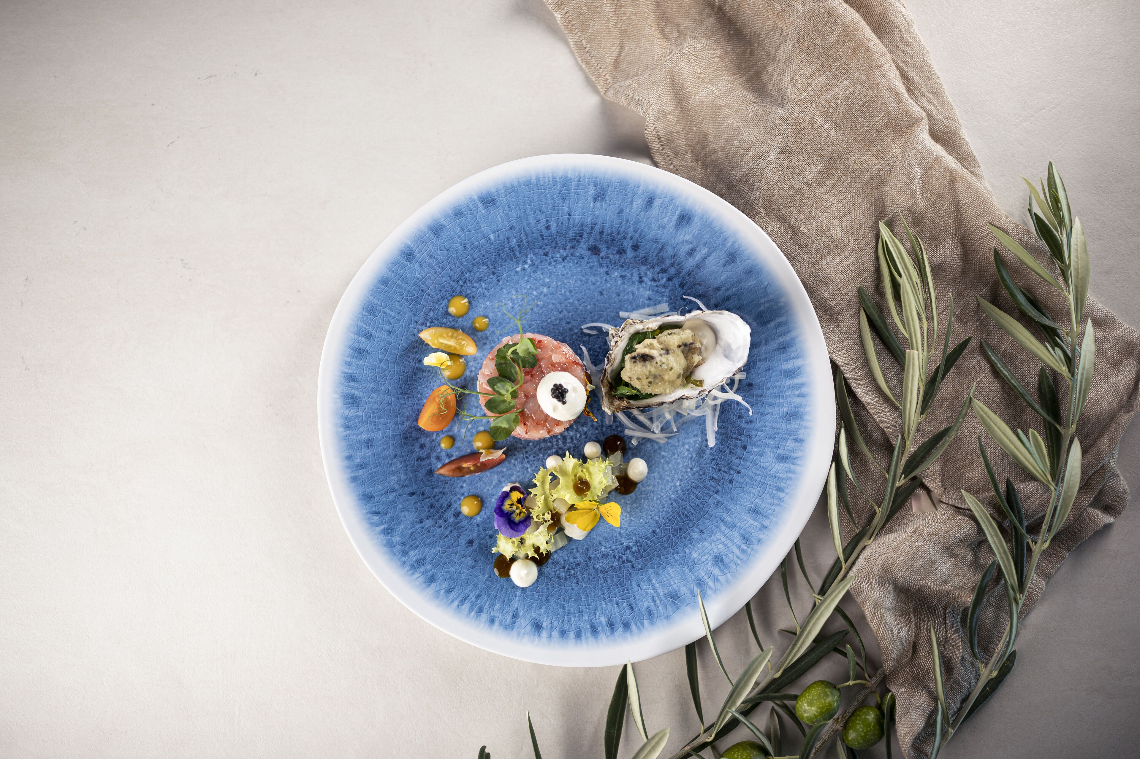 Un plato azul con diferentes alimentos y aceitunas sobre una mesa.