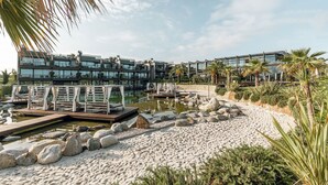 A modern hotel with a pool, palm trees, and a beach area. - Quellenhof Luxury Resort Lazise (Lazise)