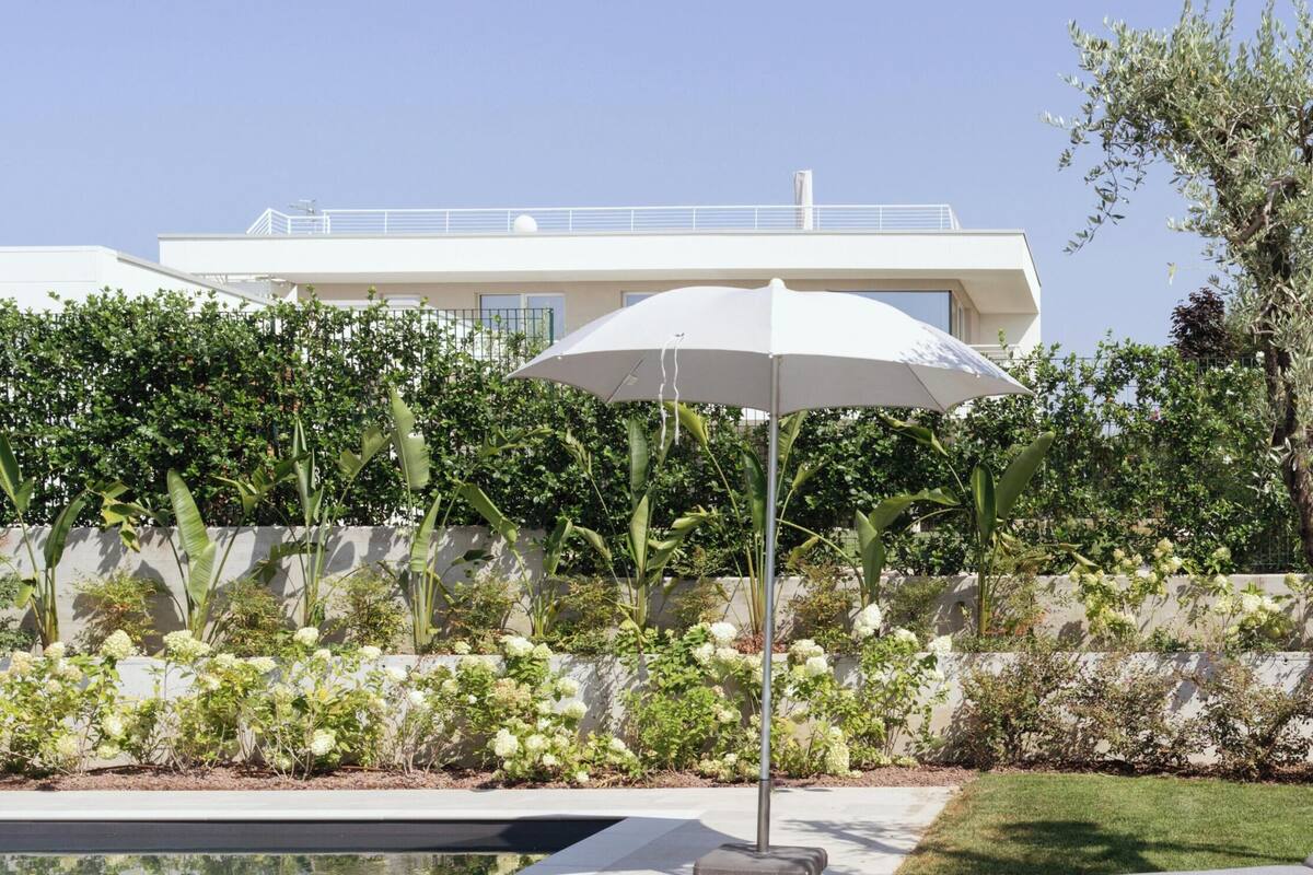 Un espacio exterior moderno con piscina, sillas de descanso y una sombrilla blanca.
