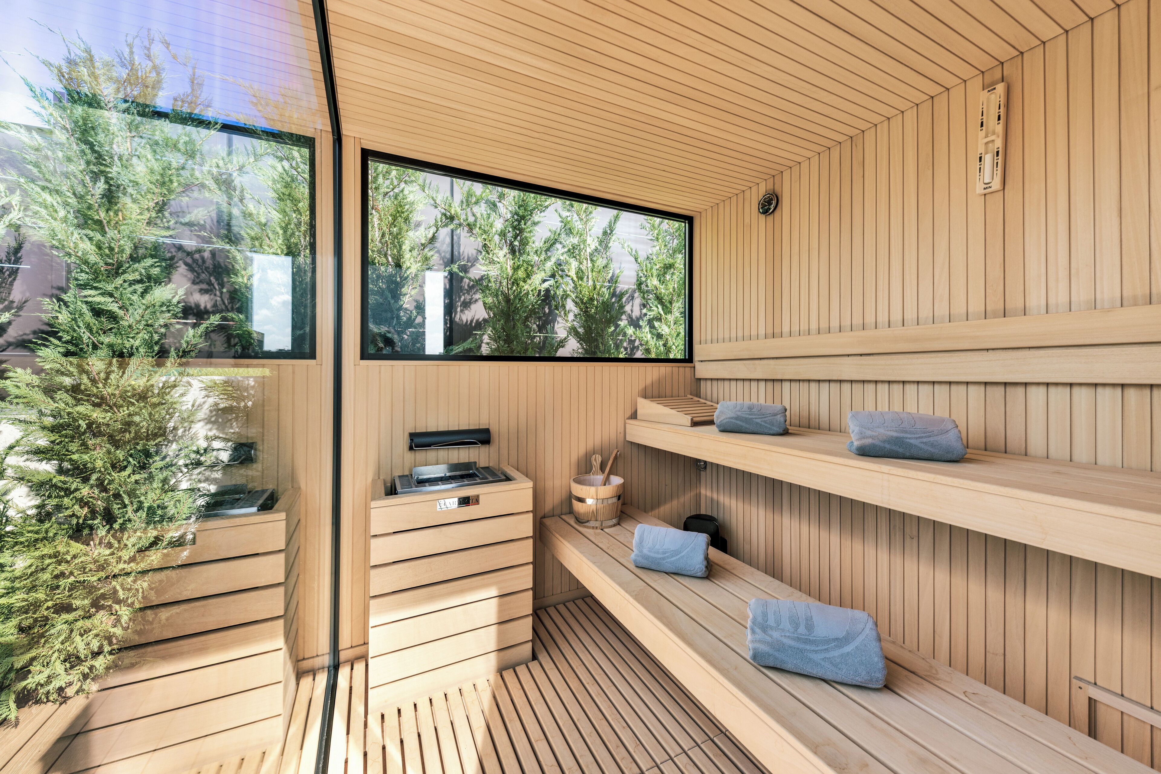 Una sauna moderna con bancos de madera, un muro de madera y una ventana que ofrece vistas a árboles.