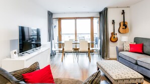 A modern living room with a flat-screen TV, a sofa, a dining area with chairs, and a guitar on the wall. - Bright, Spacious 2BR Central Cambridge Flat for 4 (Cambridge)