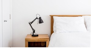 A neatly made bed with white linens, a wooden nightstand with a black desk lamp, and a white wall. - Bright, Spacious 2BR Central Cambridge Flat for 4 (Cambridge)