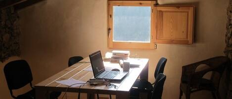 Una habitación pequeña y acogedora con una mesa de madera, una computadora portátil y sillas negras. Hay una ventana con vistas al cielo y un mueble de madera sobre la mesa.
