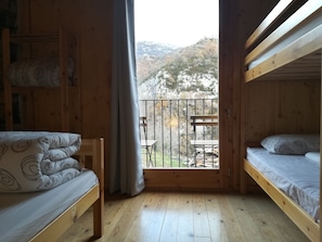 A wooden cabin with two bunk beds, a balcony with a table and chairs, and a view of a forested hillside. - Alberg Rural El Negre - Hostel (Ogassa)