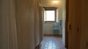 A narrow hallway with a window, a blue chair, and a wooden door. - Alberg Rural El Negre - Hostel (Ogassa)