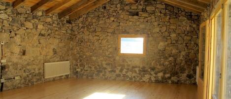 Una habitación con pared de piedra, vigas de madera, un ventanal y un radiador.