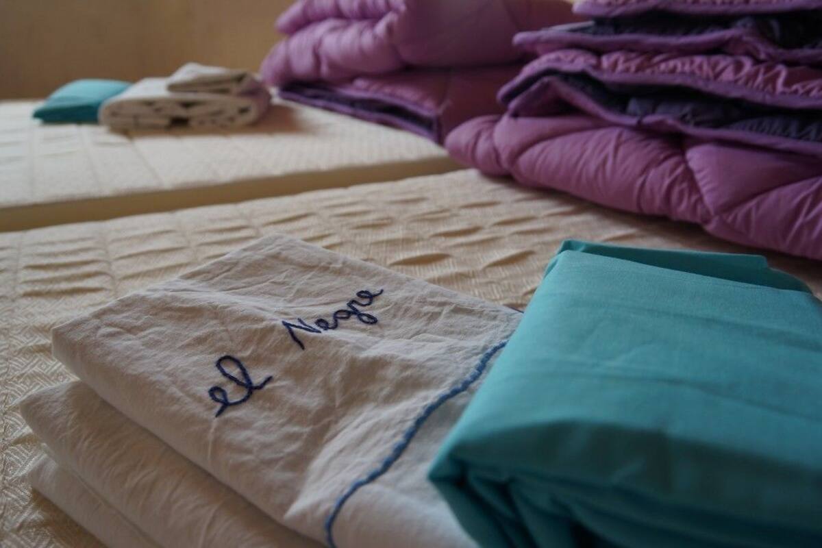 A neatly made bed with a folded white blanket and a teal pillow.