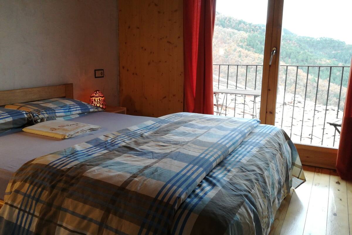 A bedroom with a bed, a nightstand, and a window with a view of a forested hillside.