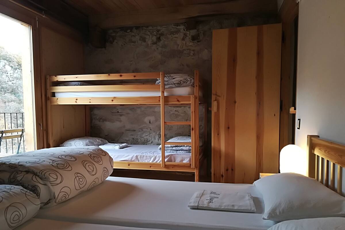 A room with two bunk beds, a wooden wardrobe, and a window with a view of trees.