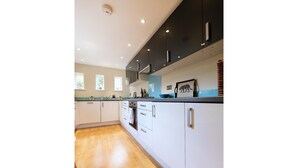 A modern kitchen with white cabinets, a wooden floor, and a framed animal picture on the counter. - Renovated House Near Antique Market (London)