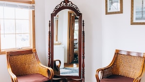 A room with two wicker chairs, a large mirror, and a hanging light fixture. - Captain's Cottage (Forked River)