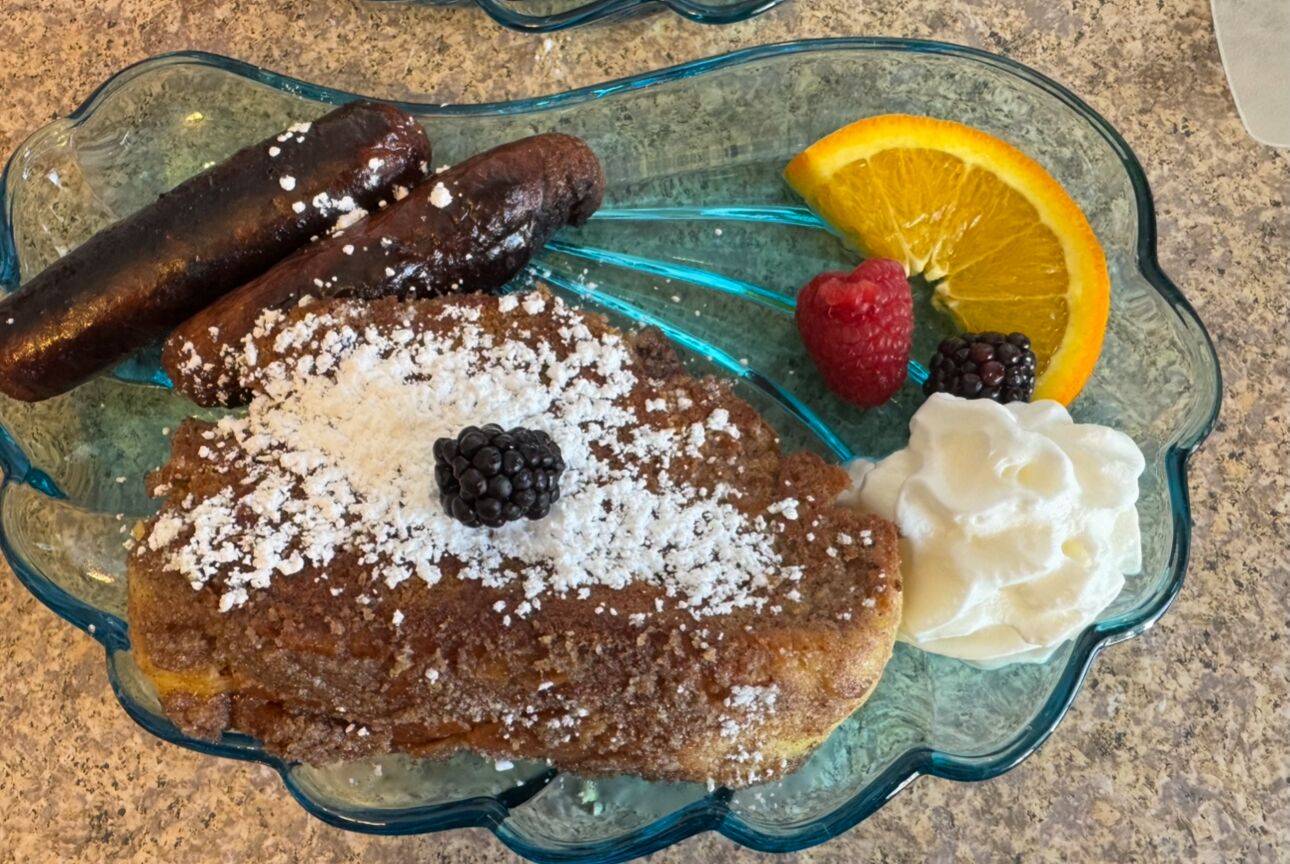Un recipiente de vidrio con tortitas, salchichas, bayas y crema batida.