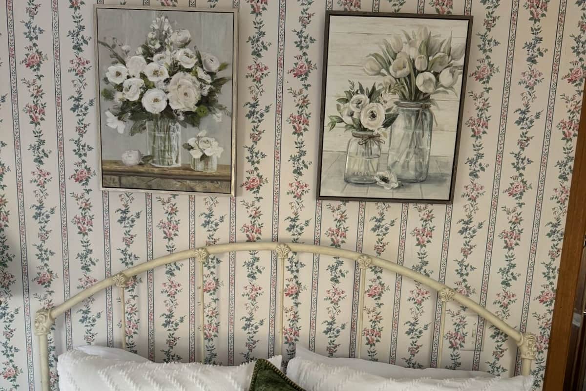 Cama com almofadas brancas e manta verde, com papel de parede estampado com flores.