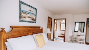 A neatly made bed with a wooden headboard, white and patterned pillows, and a painting of a beach scene above it. - Captain's Cottage (Forked River)