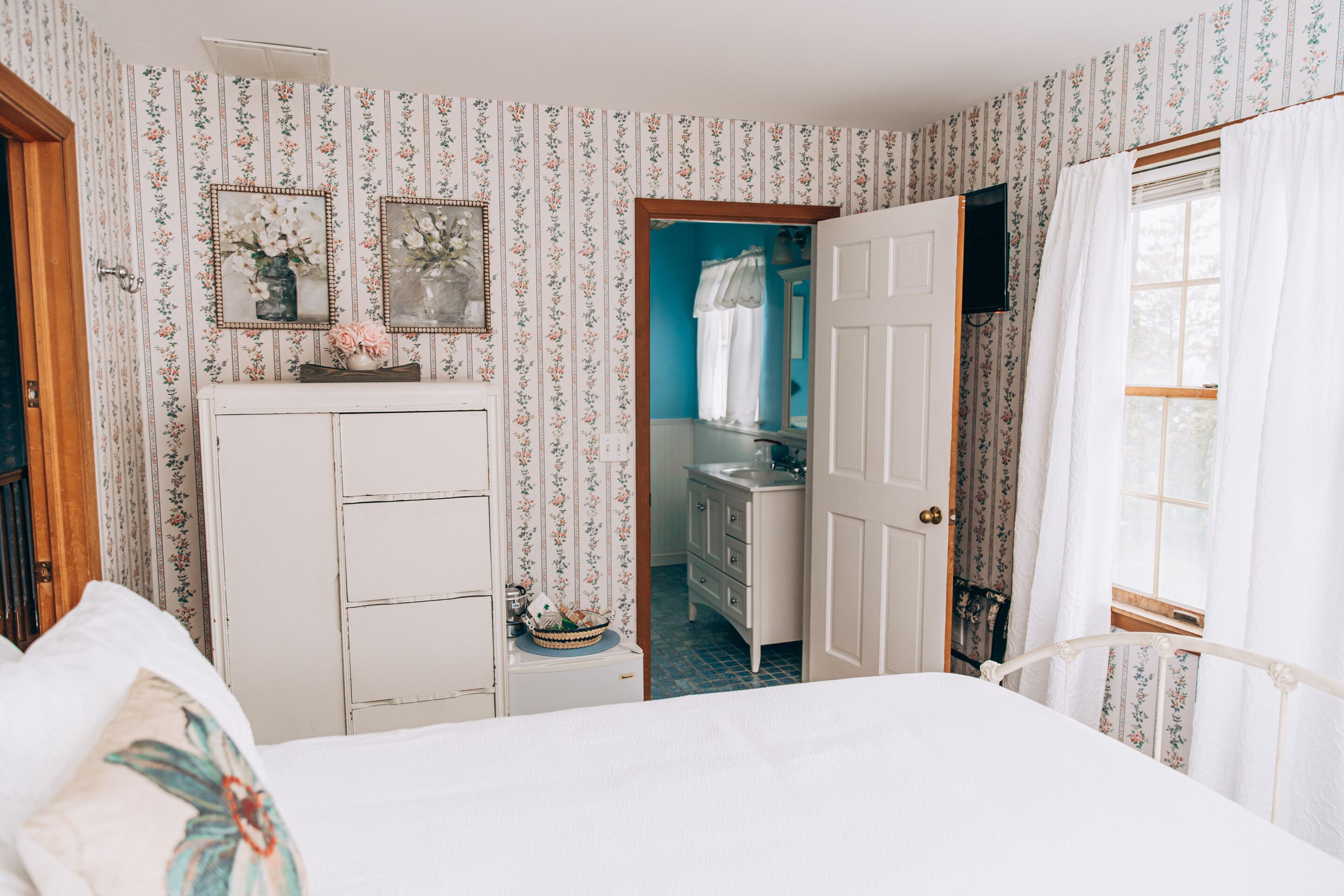 Quarto com cama, penteadeira, espelho e banheiro visível por uma porta aberta.