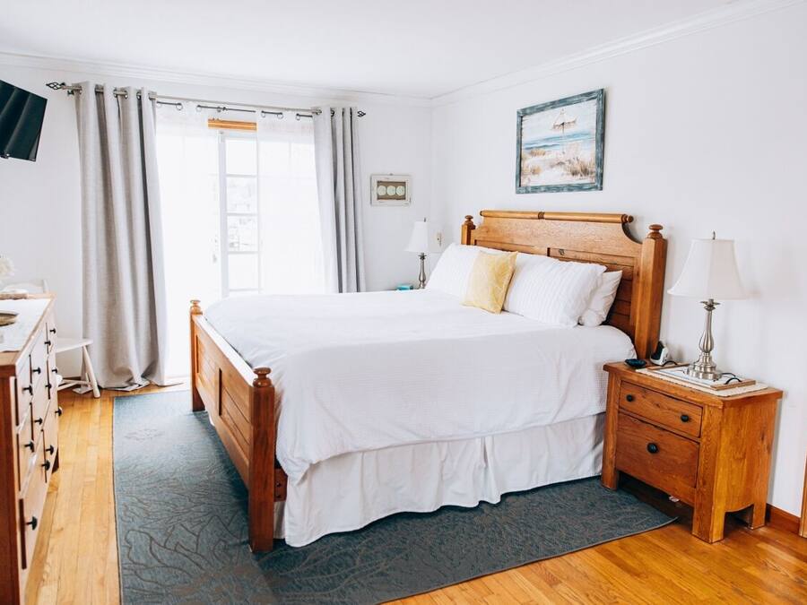 Un dormitorio con una cama de madera, una mesita de noche con lámpara, un aparador y un televisor montado en la pared.