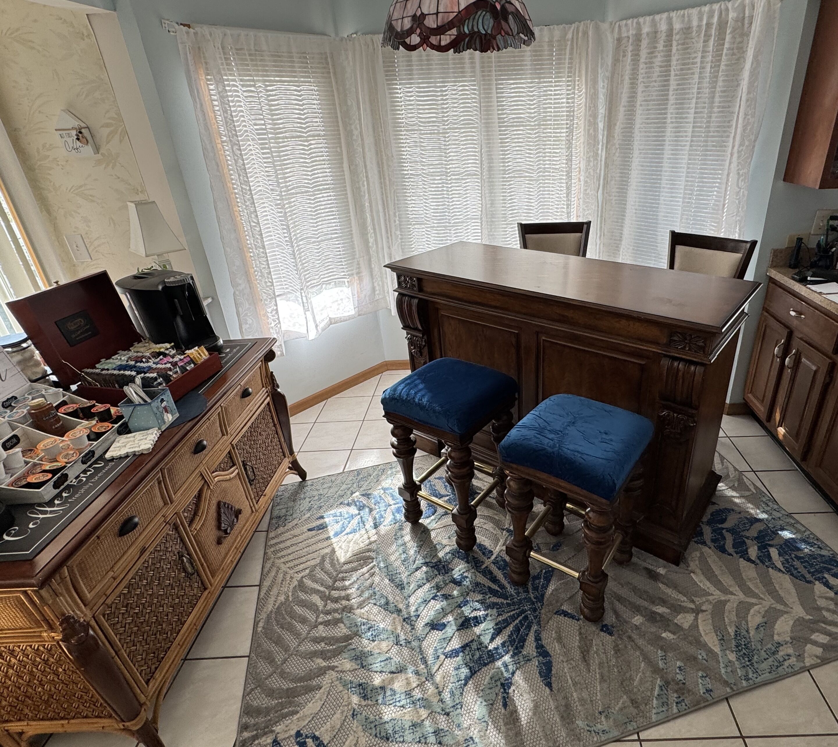 Una cocina con barra de madera, dos taburetes azules acolchados, una estación de café y baldosas de suelo estampadas.