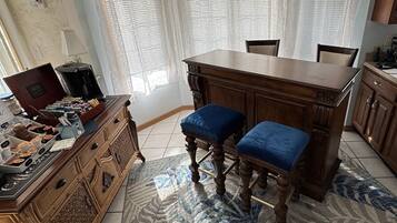 Una cocina con barra de madera, dos taburetes azules acolchados, una estación de café y baldosas de suelo estampadas.
