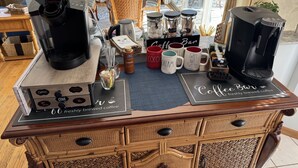 A coffee bar with a Keurig machine, various mugs, and a sign indicating it offers freshly brewed coffee. - Captain's Cottage (Forked River)