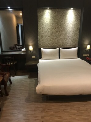 A hotel room with a large bed, a desk with a chair, a mirror, and two wall-mounted lamps. - Baseball exquisite hotel (Hsinchu)