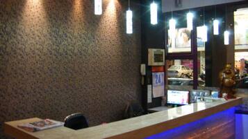 A reception desk with a patterned wall, hanging pendant lights, and a digital screen displaying information.