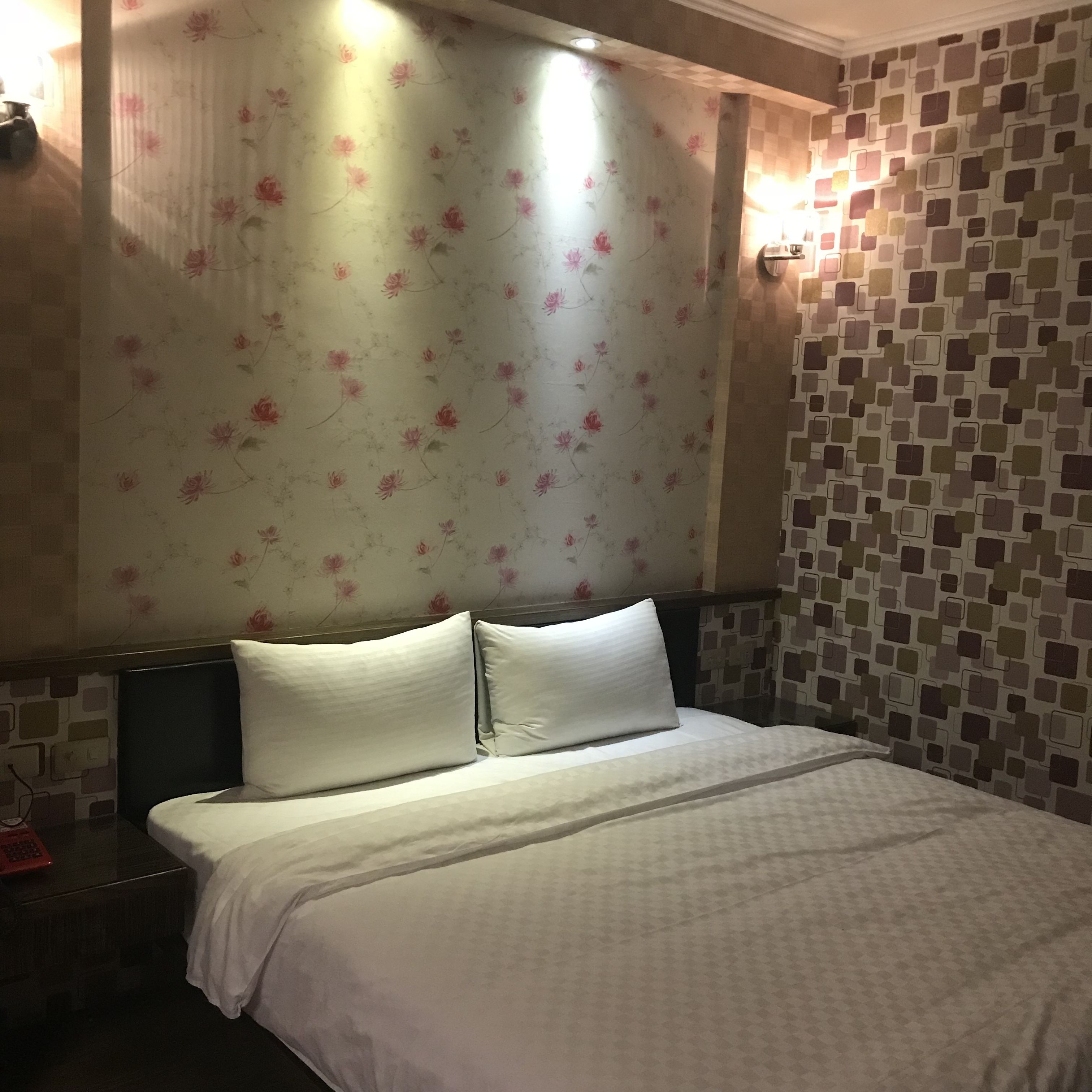 A hotel room with a bed, floral wallpaper, and a patterned wall.