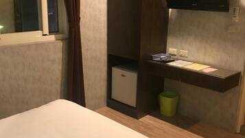 A hotel room with a bed, a small desk with a computer, a TV mounted on the wall, and a window with curtains.